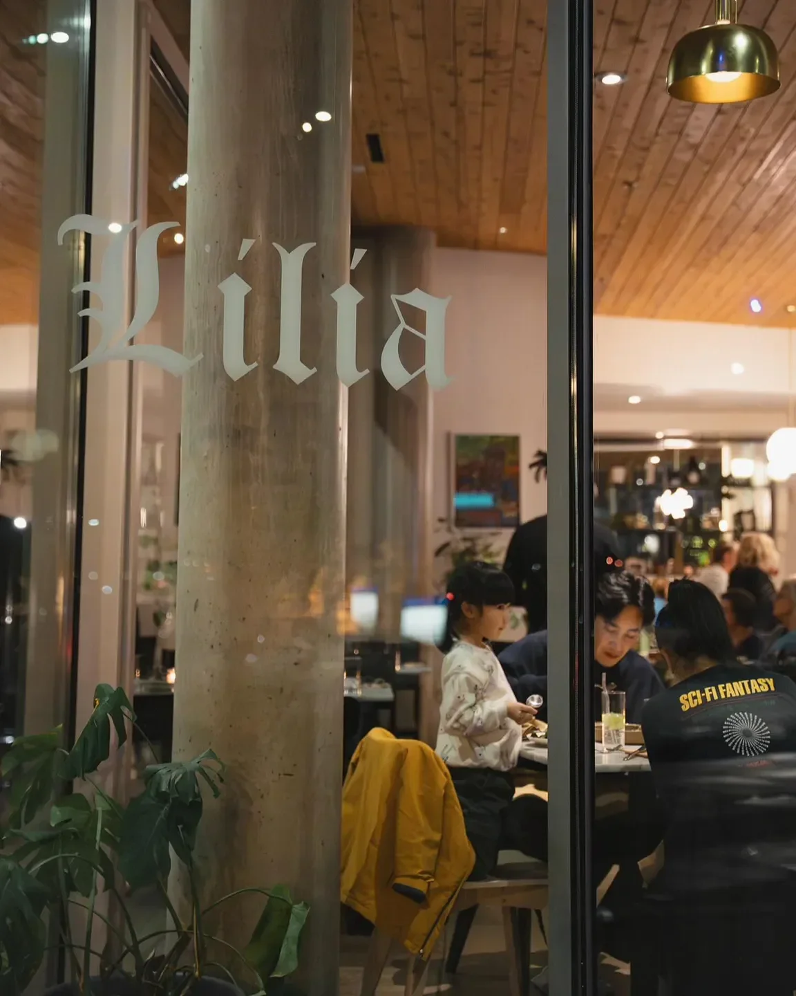 Exterior of Lilia Comedor restaurant in Portland, with customers dining inside at night.