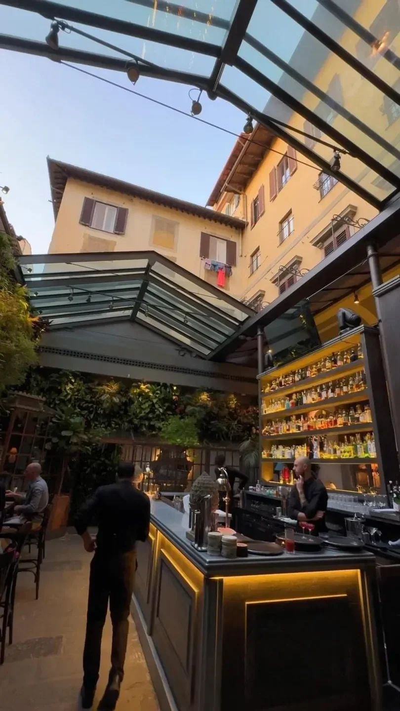 Locale Firenze in Florence: Stylish bar with a glass roof, lush plants, and a well-stocked bar.
