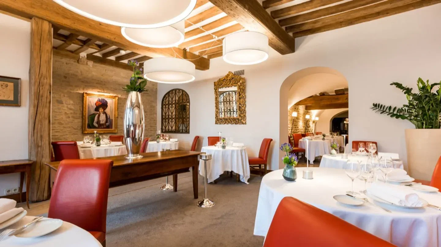 Elegant dining room at Maison Lameloise in Bourgogne, with white tablecloths and red chairs.