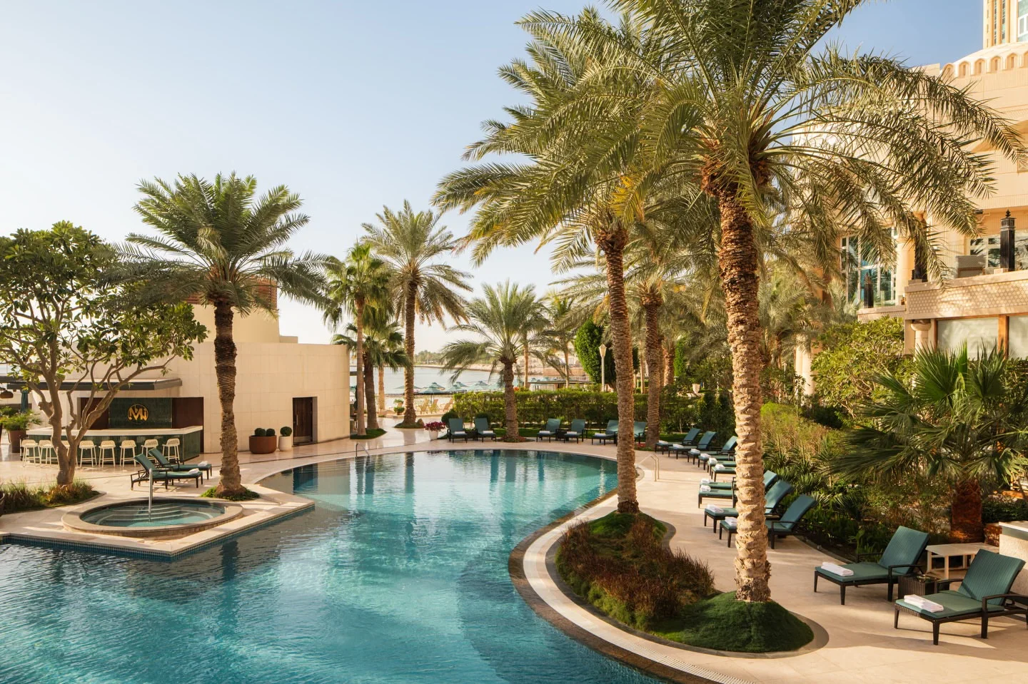 Makani Beach Club in the city features a luxurious outdoor swimming pool surrounded by palm trees and lounge chairs.