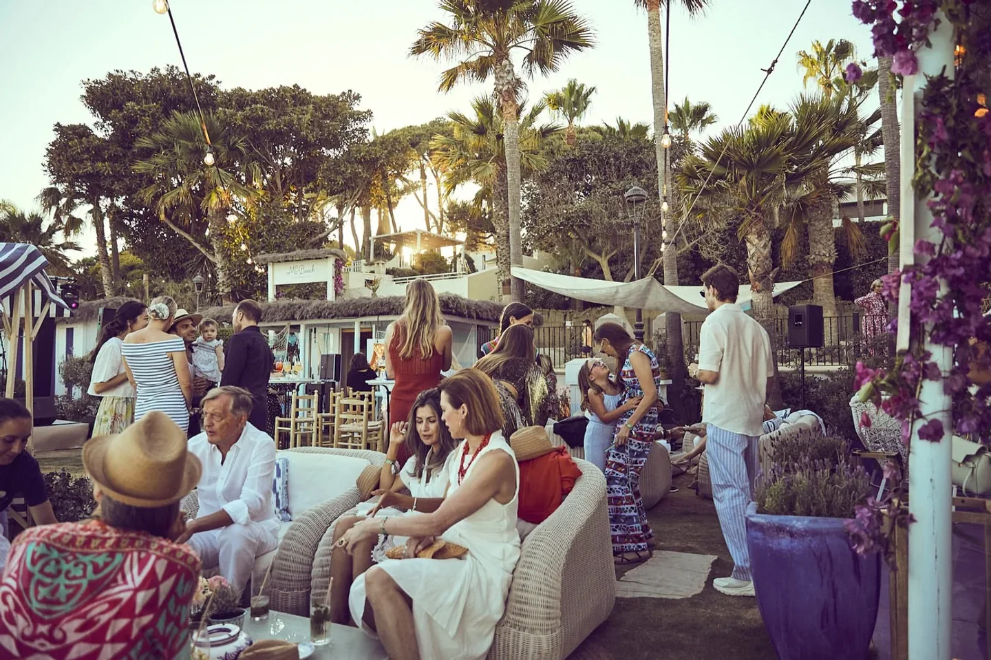 People mingling at Marbella Club Beach Club in Marbella during a summer evening event with palm trees and outdoor seating.