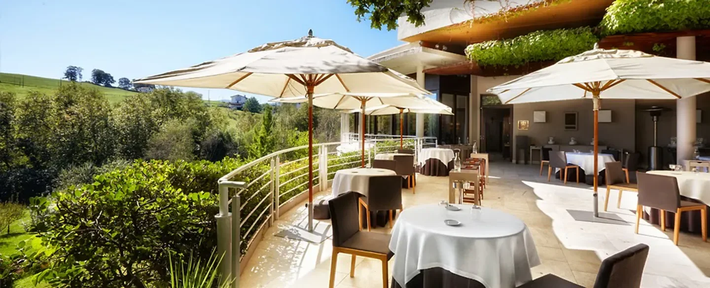Outdoor dining at Martín Berasategui in San Sebastian with scenic views and umbrellas.