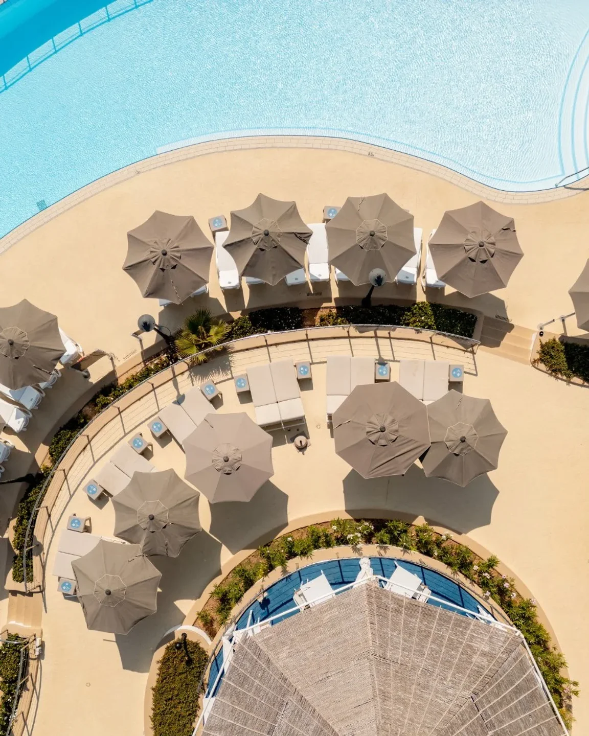 Aerial view of Merkanti Beach Club in Malta featuring a large swimming pool and numerous umbrellas over loungers.