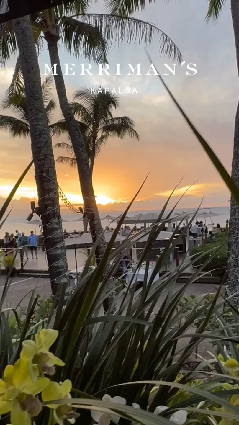 Sunset over Merriman's Kapalua restaurant in Maui, with palm trees and ocean views.