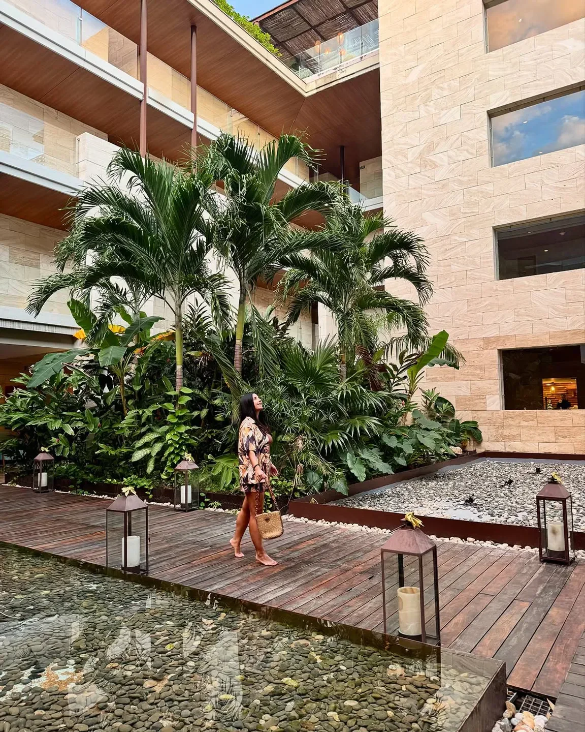 Woman walking at Mio restaurant in Hanoi, with wooden deck, water feature and greenery.