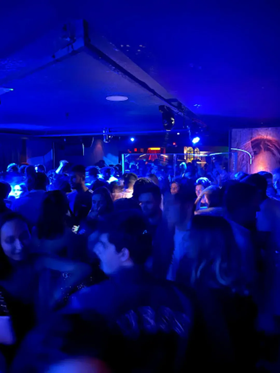 Energetic crowd enjoying a night out at MYMO nightclub in Madrid, bathed in blue light.