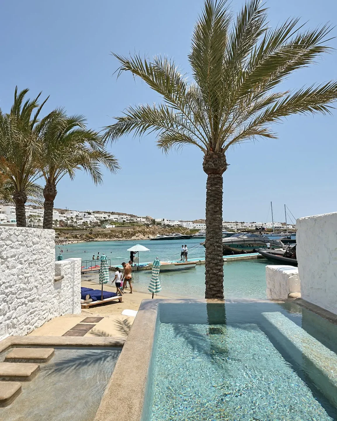 Private pool and beach at Nammos Mykonos, featuring palm trees and clear turquoise waters.