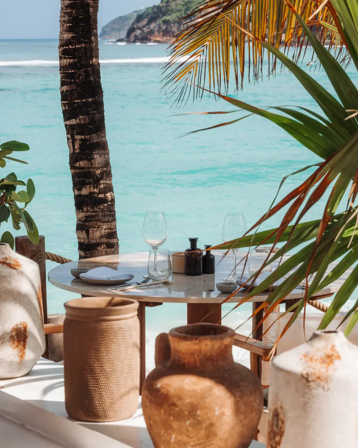 Table set at Nao Beach restaurant in St. Barts with ocean view and palm fronds.