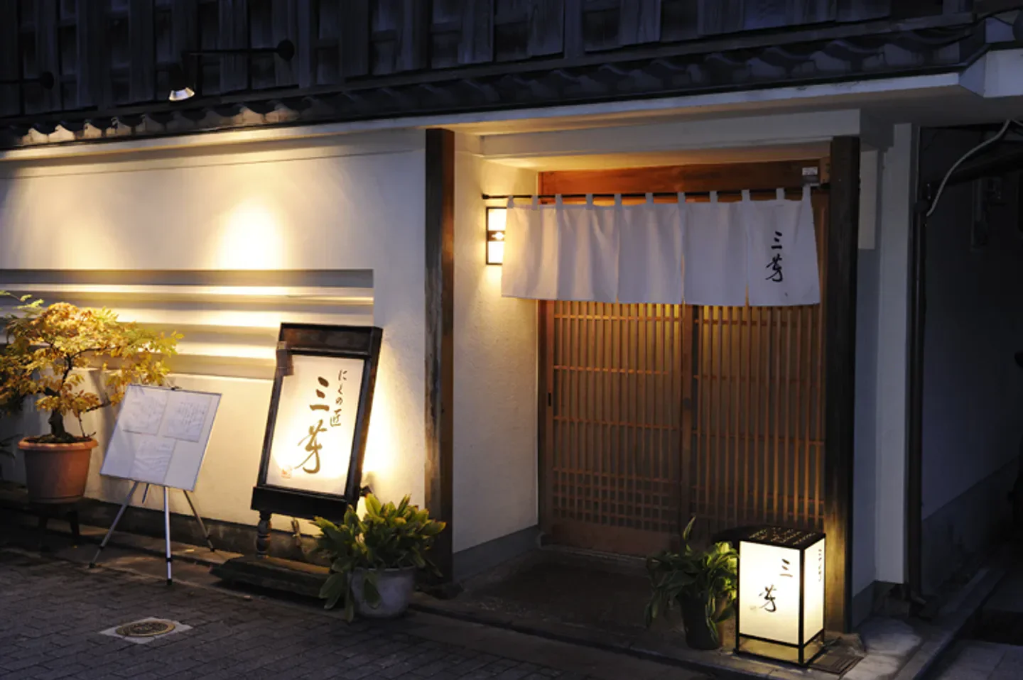 Entrance of Nikunotakumi Miyoshi restaurant in Kyoto, Japan, with traditional design and lighting.