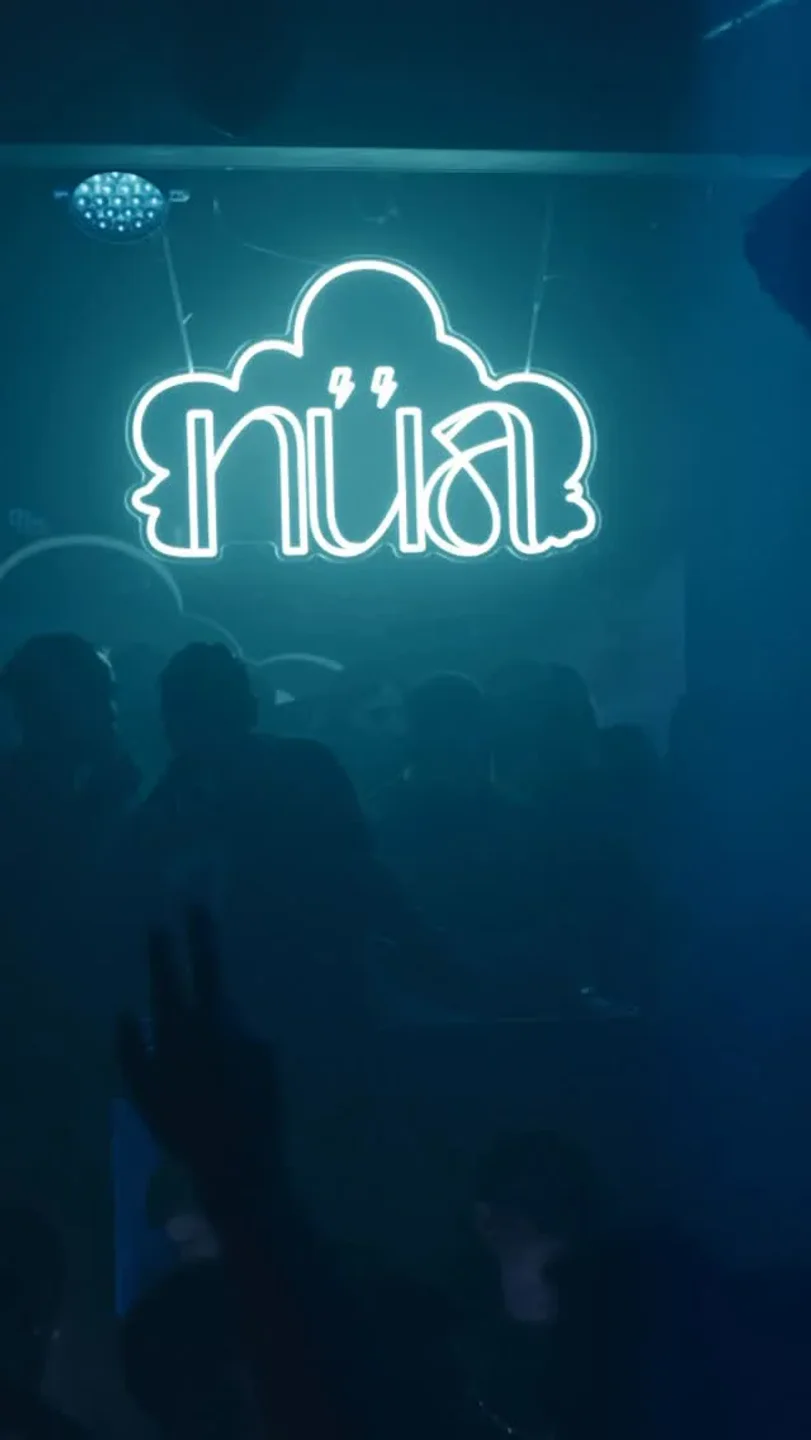 Neon Nua logo illuminates the dark ambiance of the nightclub in the city, with silhouettes of people dancing.