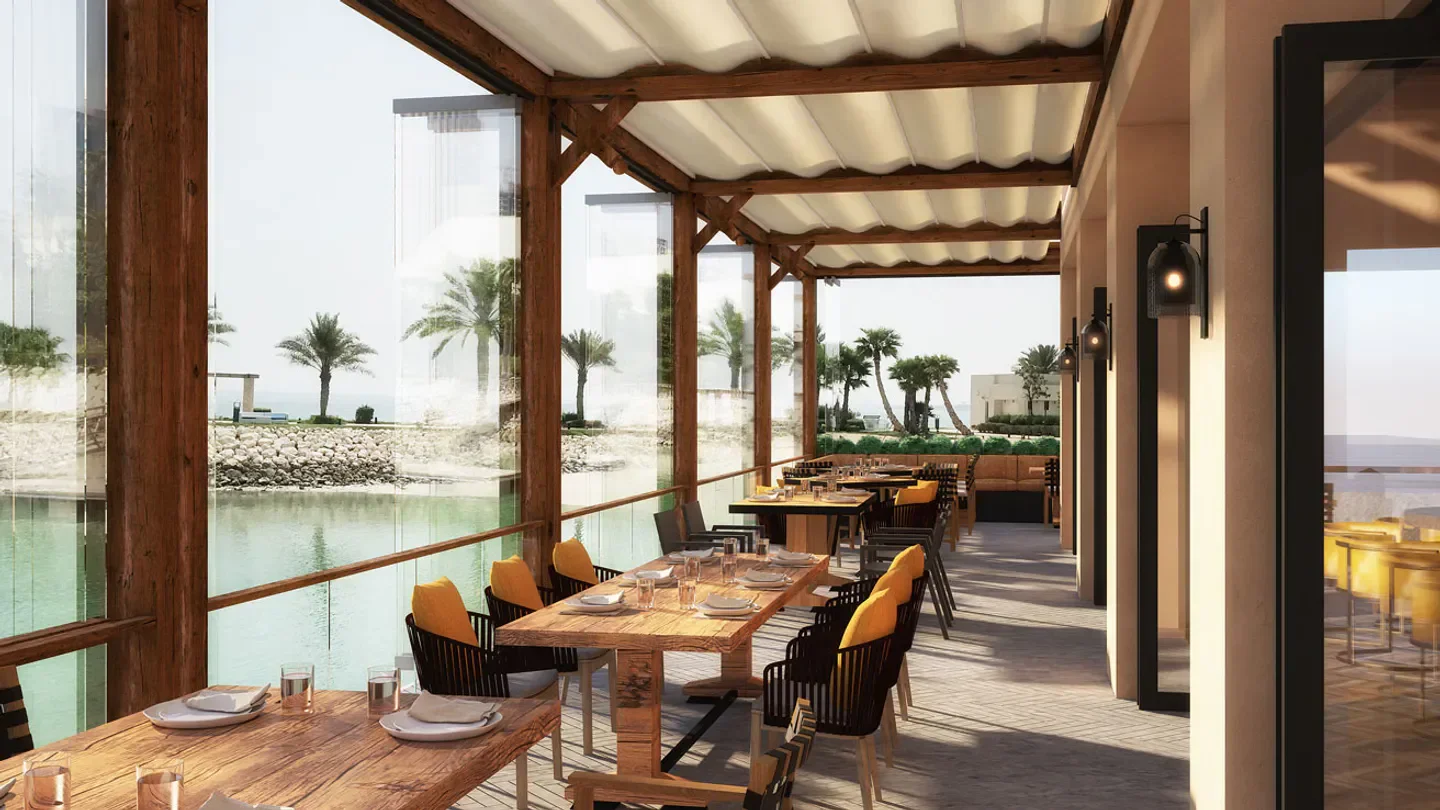 Outdoor dining at Nusr-Et Steakhouse in Doha, overlooking the water with palm trees.