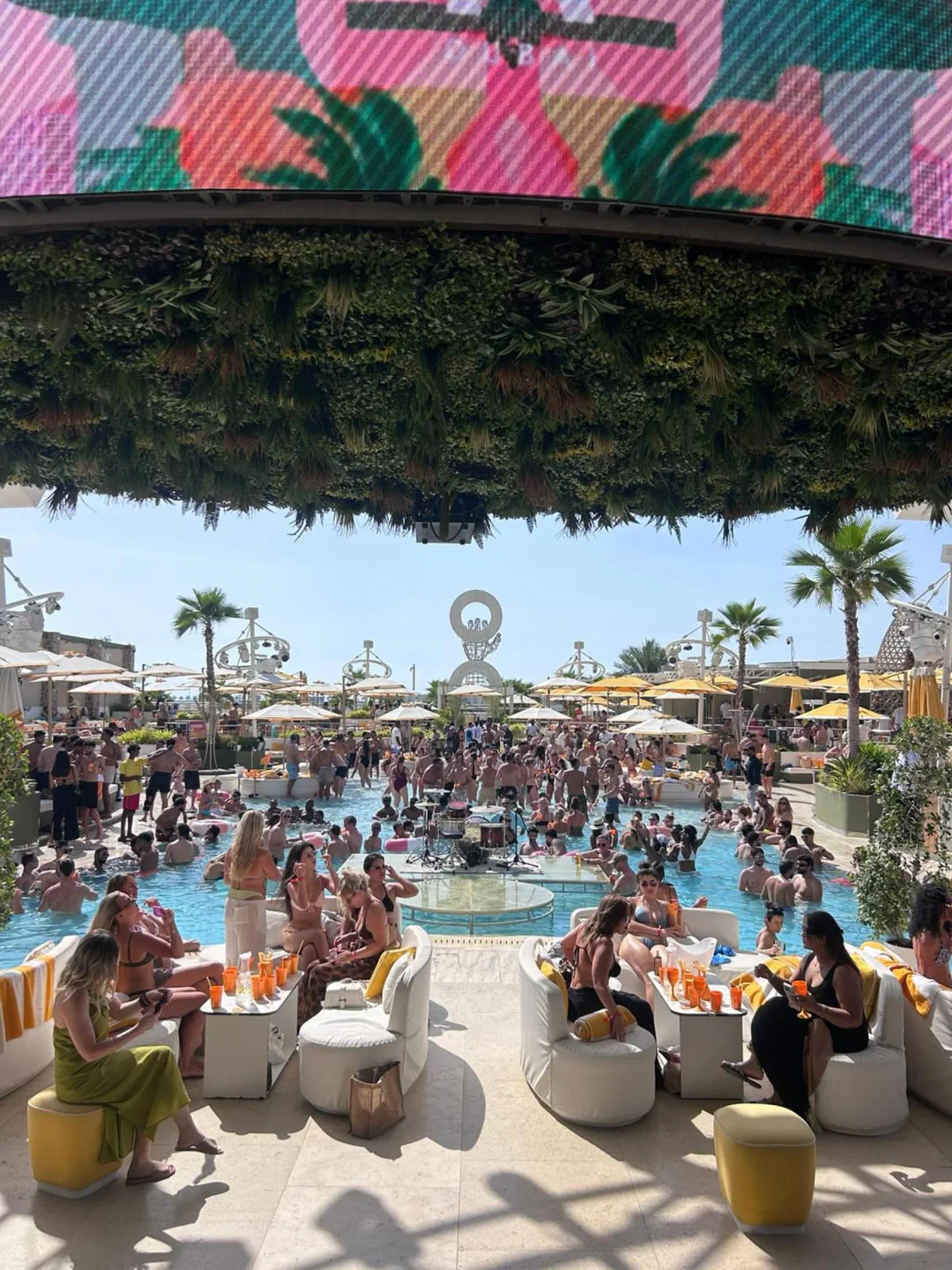 O Beach pool party with people enjoying drinks and music under a sunny sky in the city