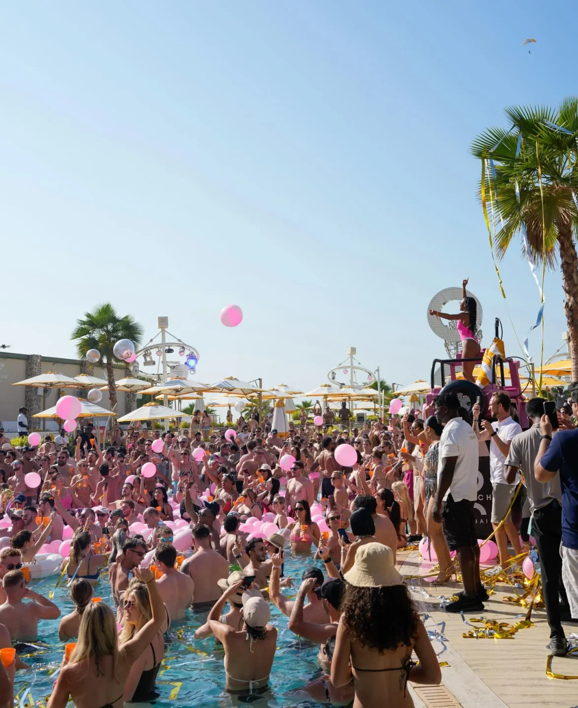 O Beach pool party in the city with a crowd celebrating and pink balloons floating