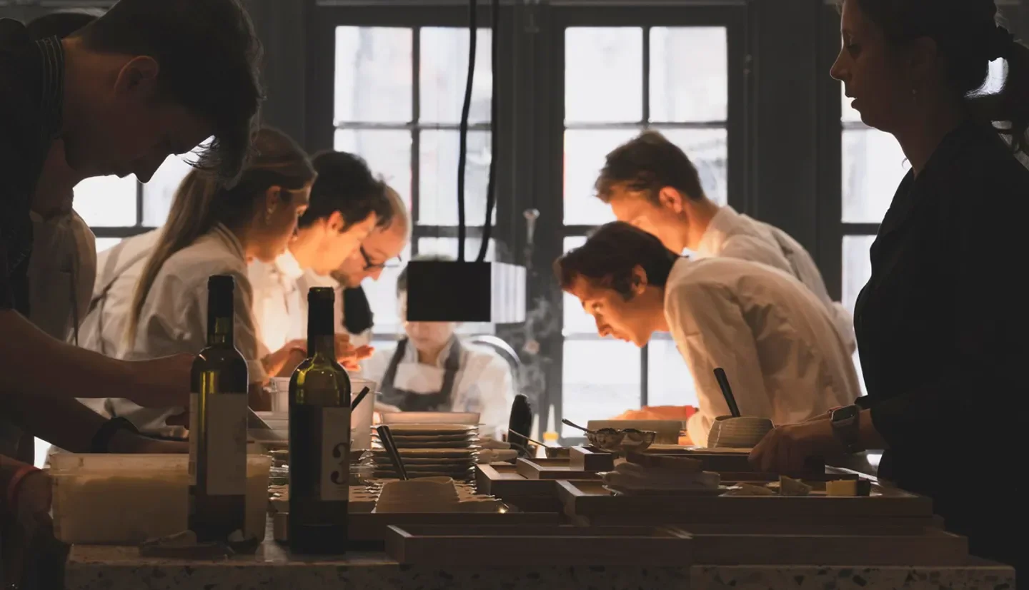 Chefs preparing food at OAK restaurant in Ghent, Belgium, with wine bottles in the foreground.