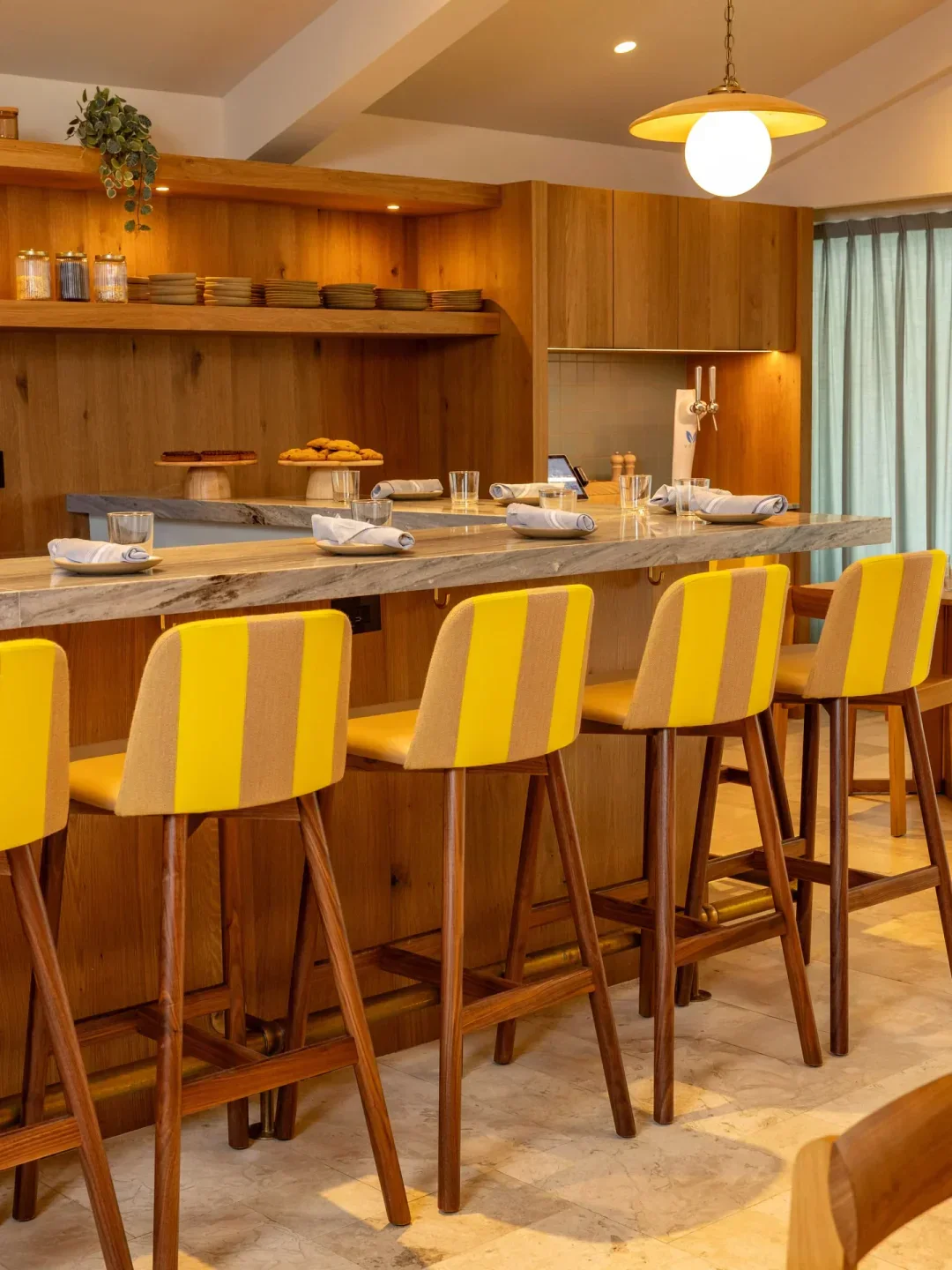 Interior of Oceano Kitchen in Palm Beach, featuring bar with yellow chairs and wooden decor.
