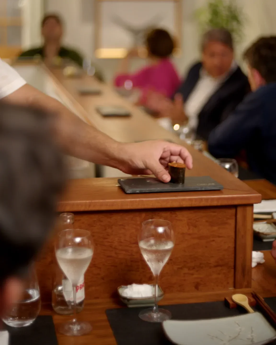 Serving sushi at Oizumi Sushi in Sao Paulo, with sparkling wine and dining patrons.