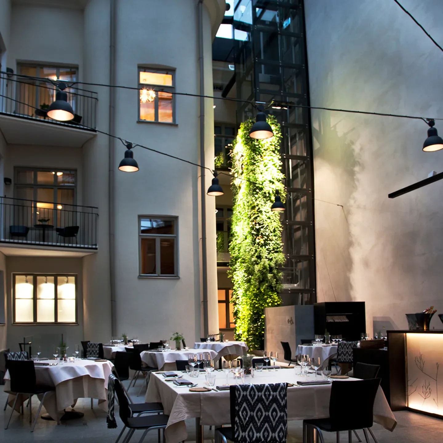 Elegant courtyard dining at Olo restaurant in Helsinki, Finland. Tables set with hanging lights.