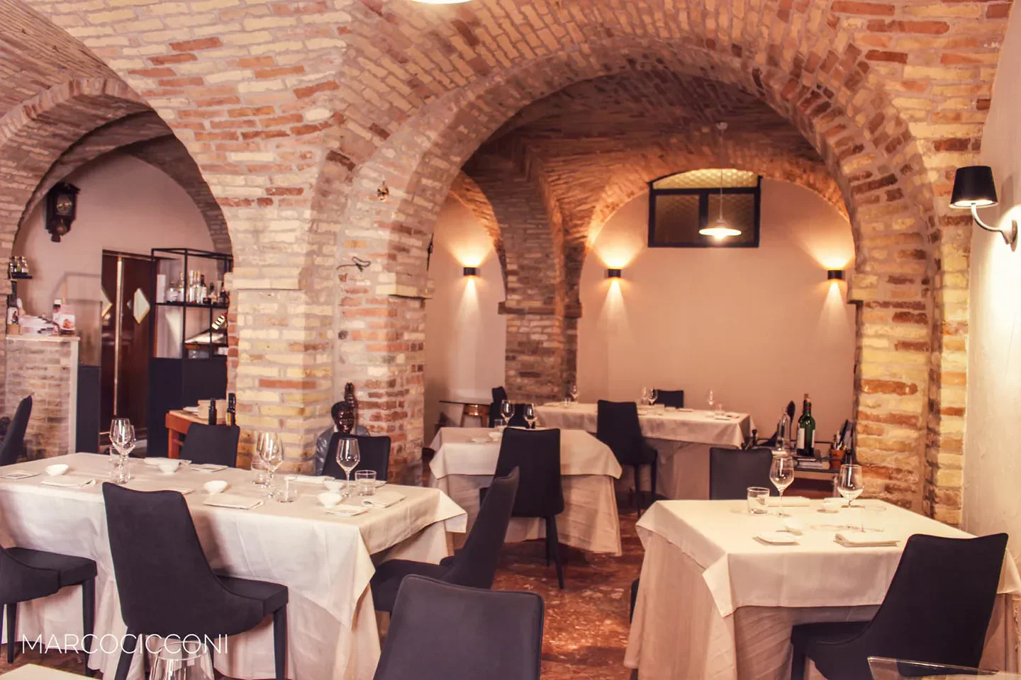 Interior of Osteria Ophis restaurant in Marche, featuring brick arches and elegant dining tables.
