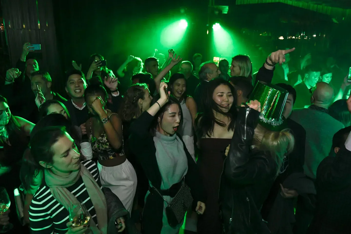 Energetic crowd partying at Ozone nightclub in Hong Kong, lit by green lights.