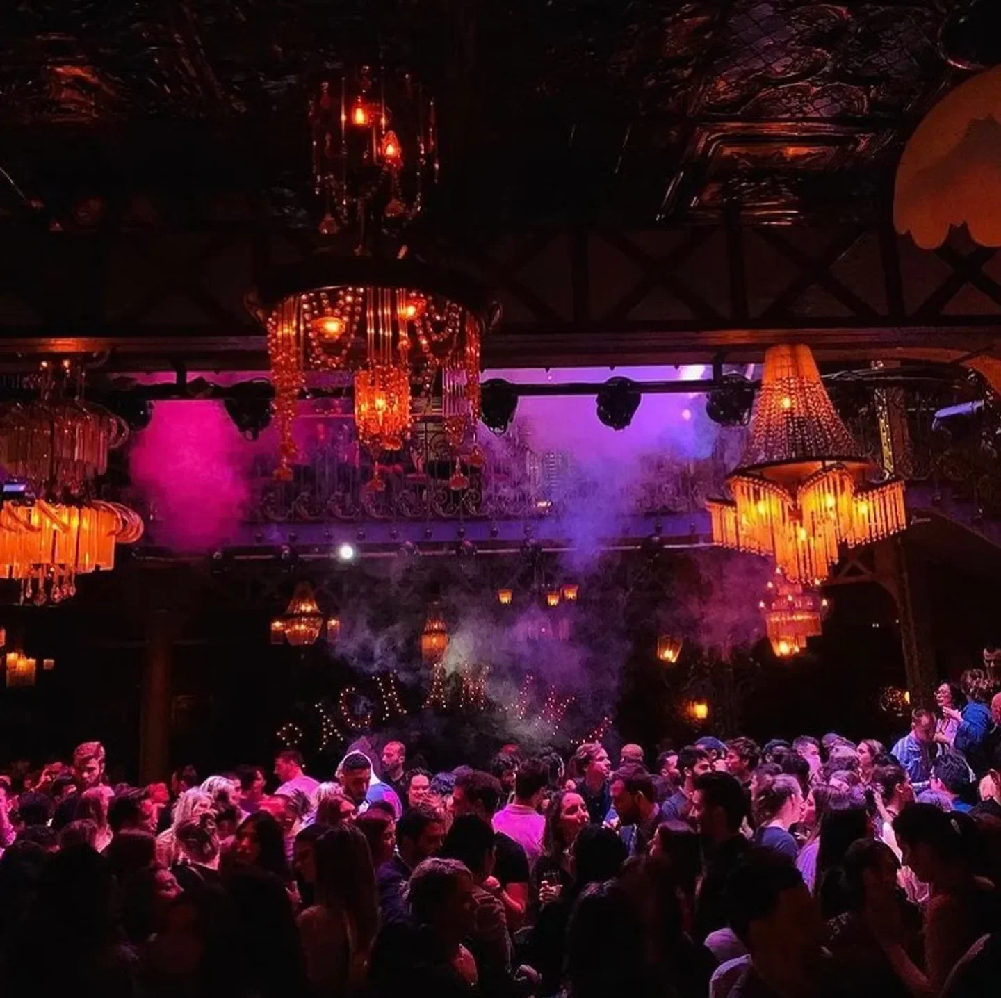 Inside Pachamama nightclub in Paris, with people, chandeliers, and purple stage lighting.