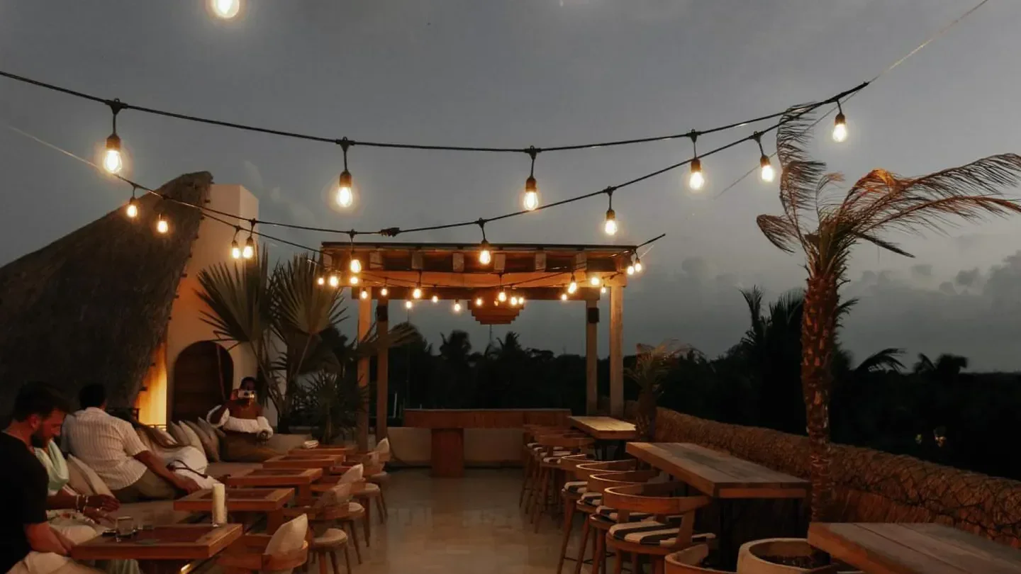 Rooftop terrace at Panamera Beach Club in Tulum, string lights and palm trees.