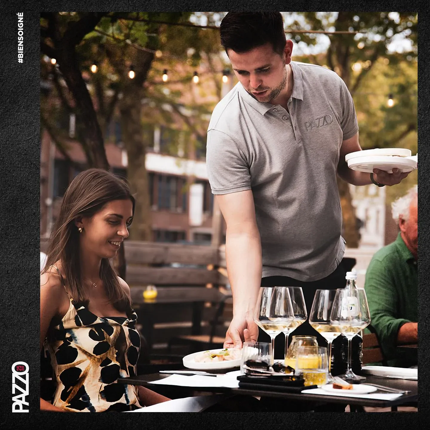 Server at Pazzo restaurant in Antwerp serving plates to a customer outdoors.