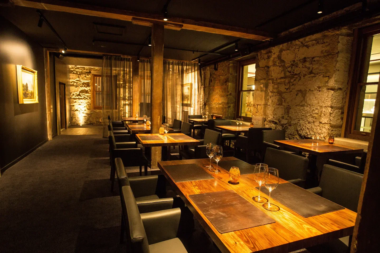 Cozy dining area at Peacock and Jones restaurant in Hobart, featuring wooden tables and stone walls.