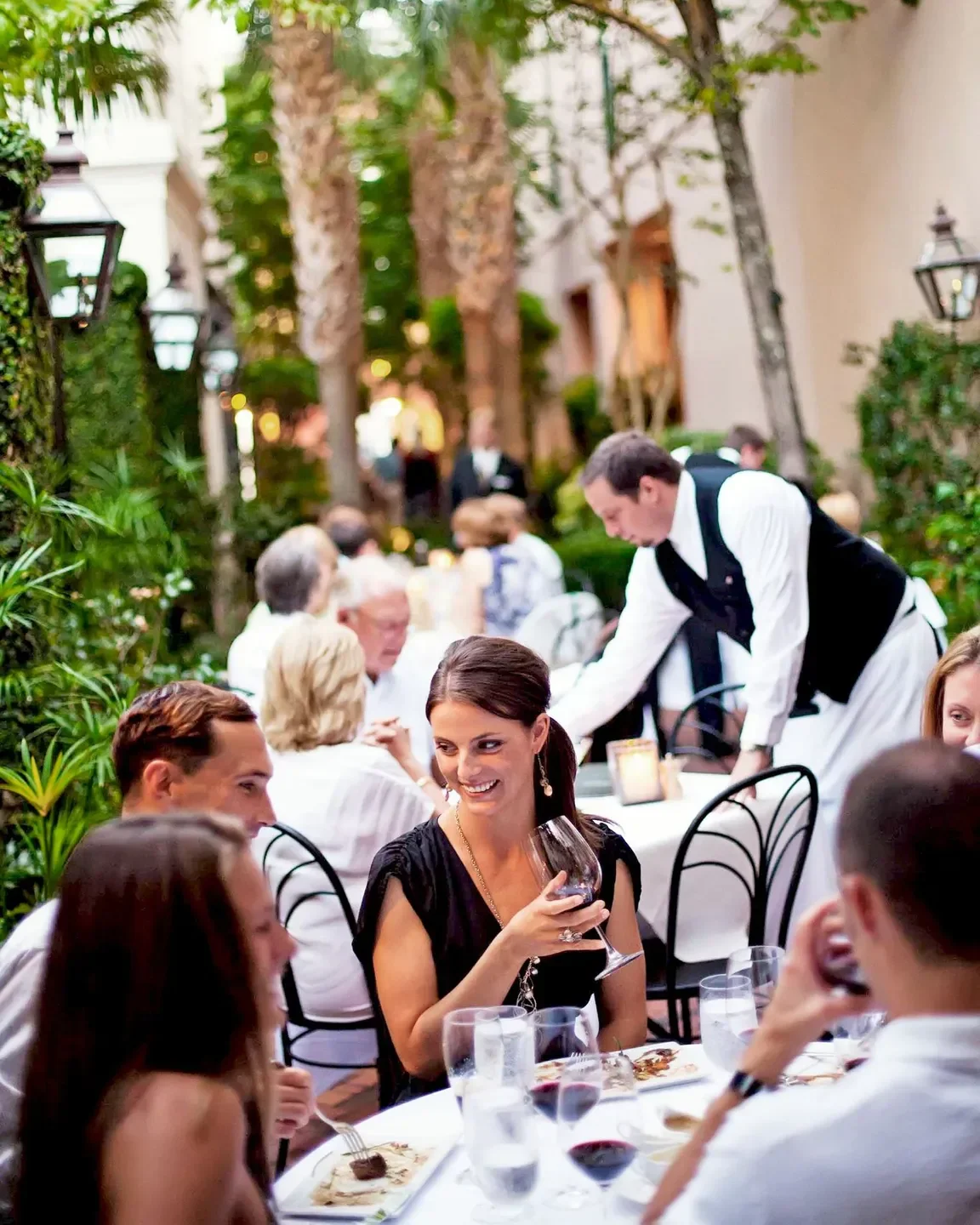 Outdoor dining at Peninsula Grill in Charleston, featuring a waiter serving guests.
