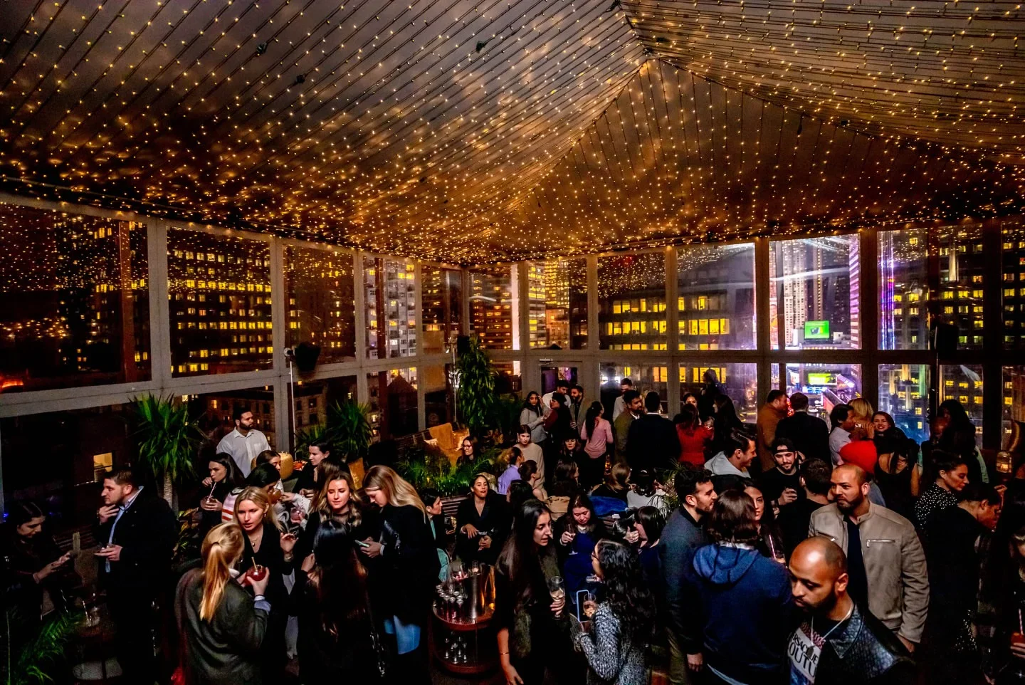 Lively crowd at PHD Midtown rooftop bar in New York City under starry string lights