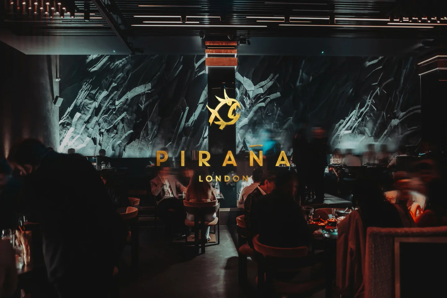 The stylish interior of PIRANA London restaurant featuring a dramatic wall art and illuminated seating area.