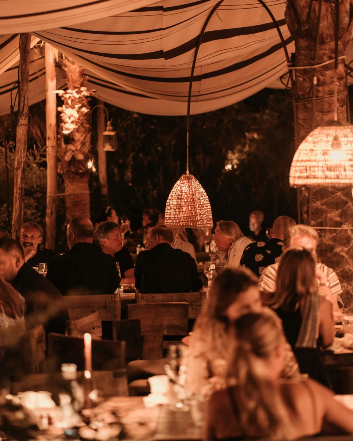 Warm, ambient lighting illuminates diners at Playa Soleil, a vibrant nightclub in Ibiza with unique woven lamps.