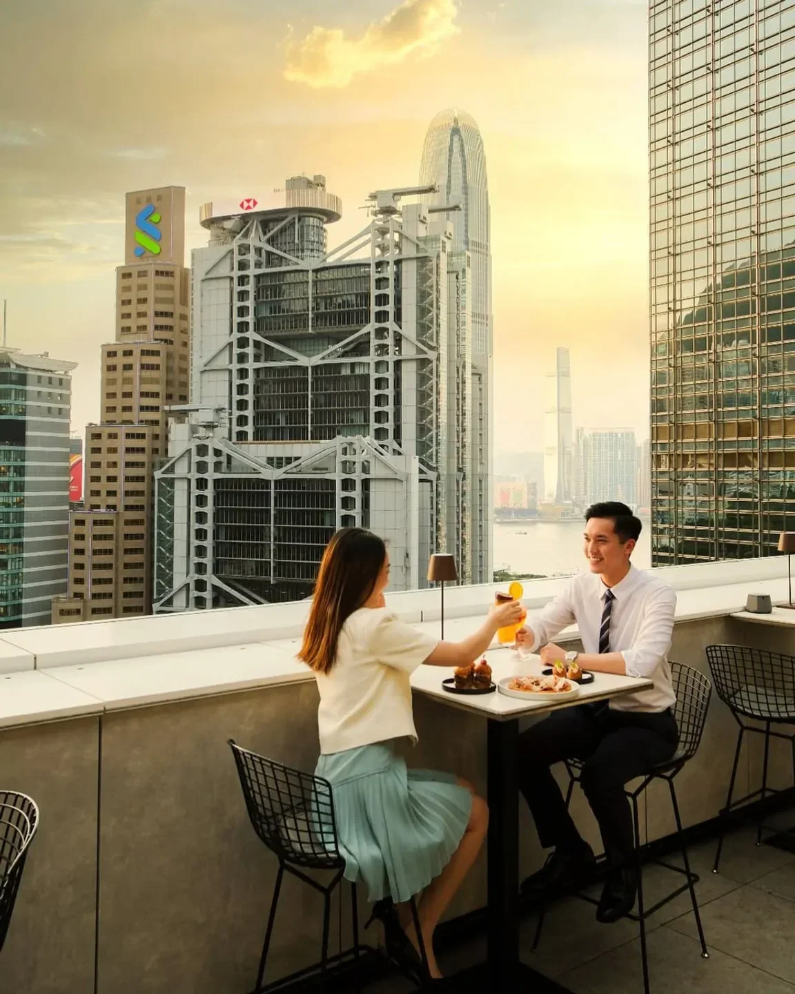 Couple toasting at Popinjays restaurant in Hong Kong, overlooking cityscape at sunset