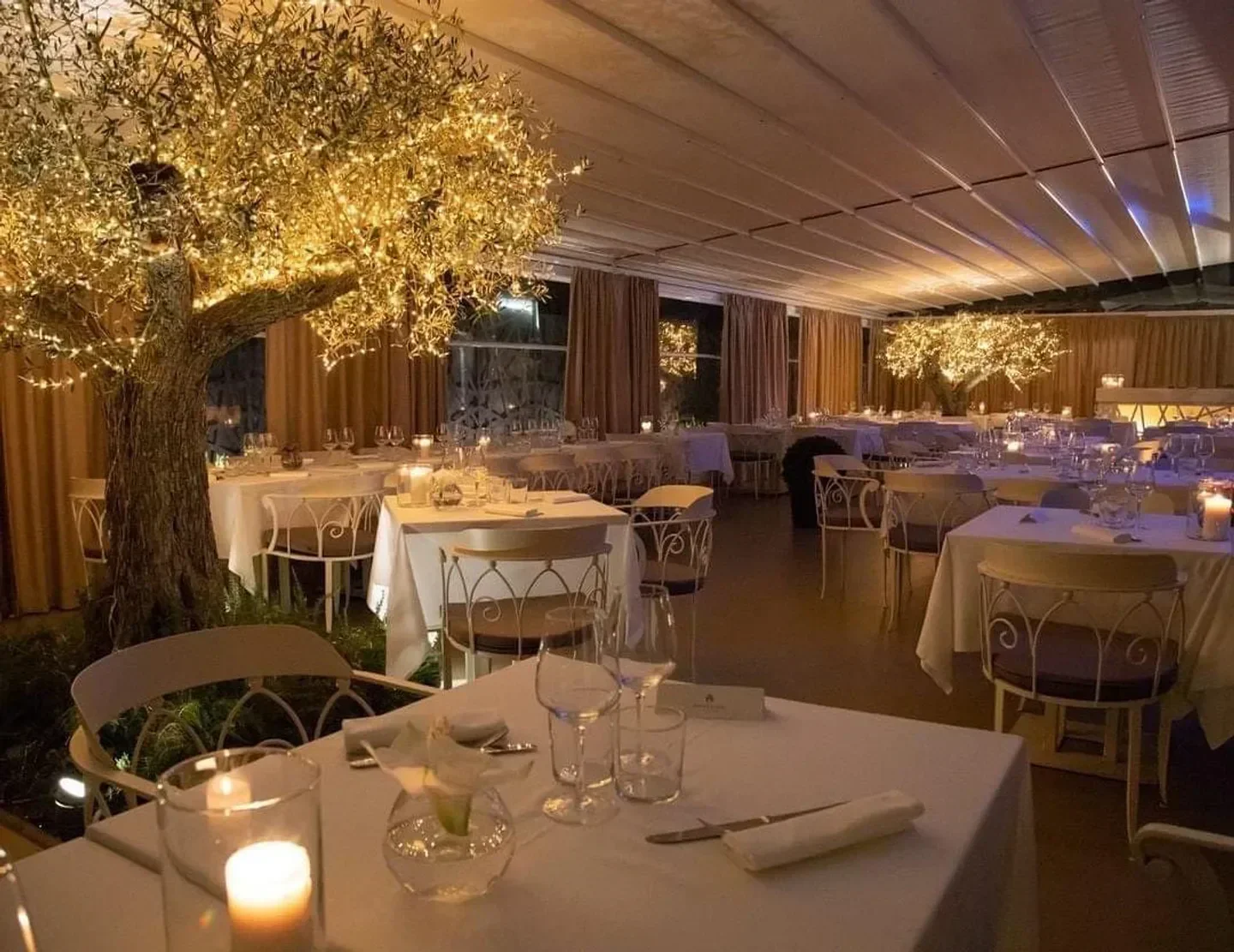 Cozy dining room at Profumo Spazio Sensoriale in Rome, with elegant tables and lit tree.