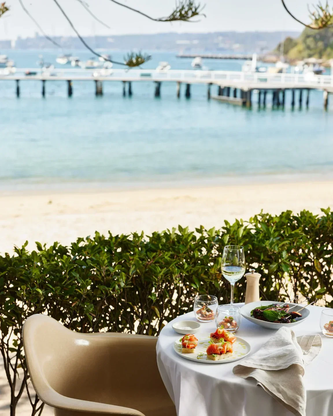 Table set at Public Dining Room in Sydney, with food, drink, and beach views.