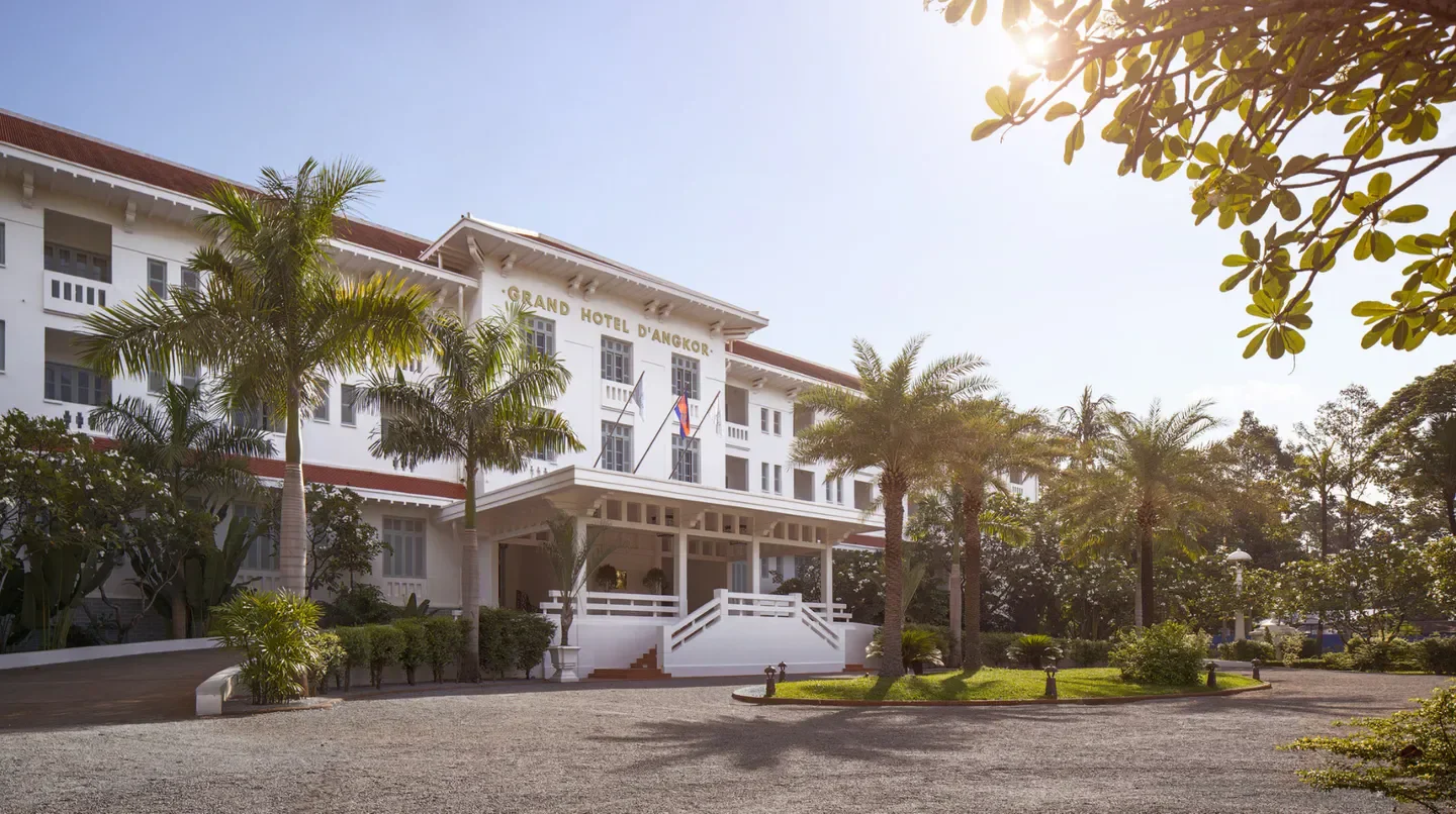 Exterior of Raffles Grand Hotel d'Angkor in Siem Reap, with palm trees and sunny skies.