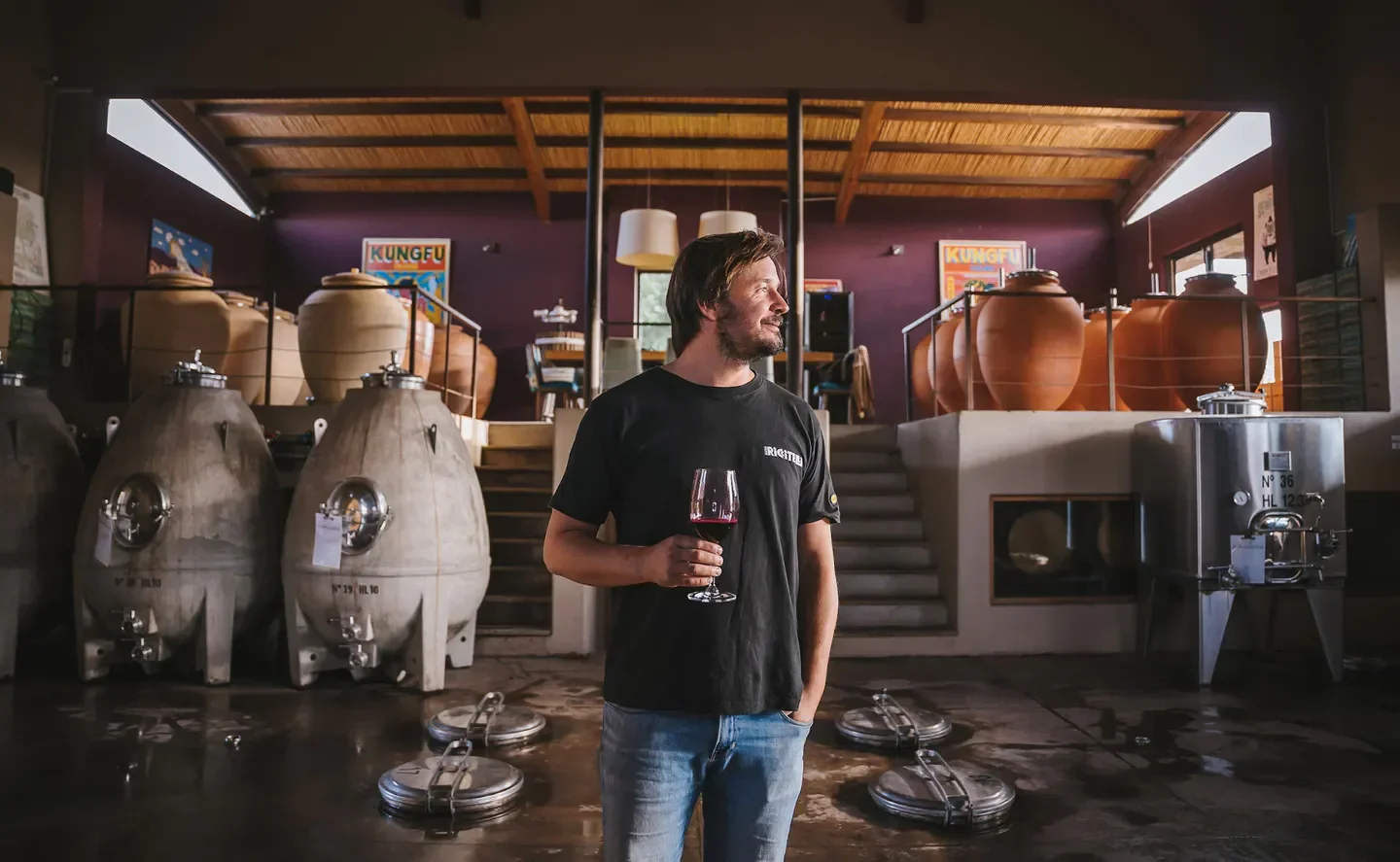 Man holding wine glass at Riccitelli Bistró in Mendoza, among wine tanks.