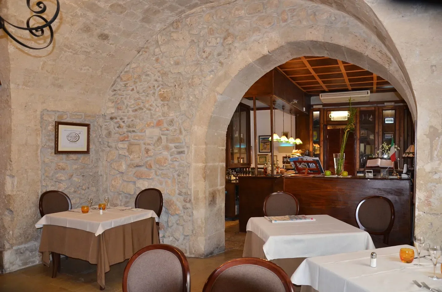 Interior view of Ristorante Don Camillo in Syracuse, showing arched doorway and stone walls.