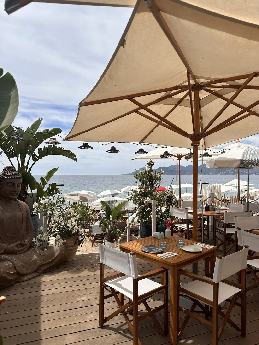 Outdoor dining at Riviera Beach in Cannes, with beach view and Buddha statue.