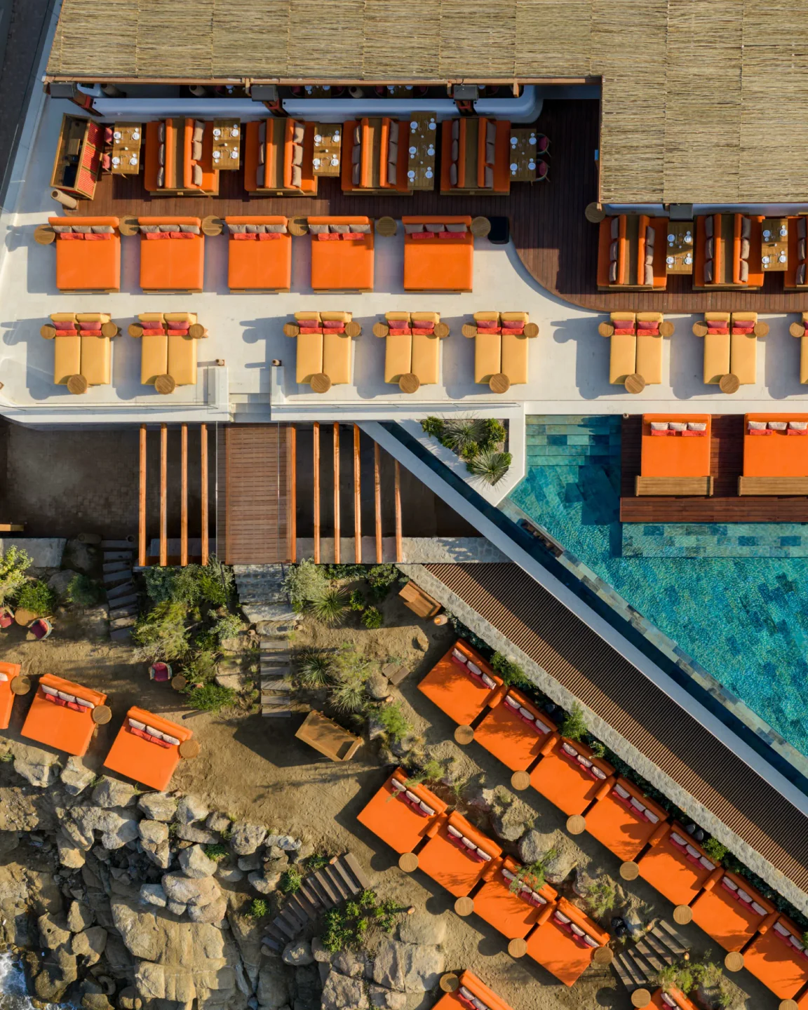 ROKA restaurant in Mykonos features a stunning poolside and dining area with orange lounge chairs and wooden accents.