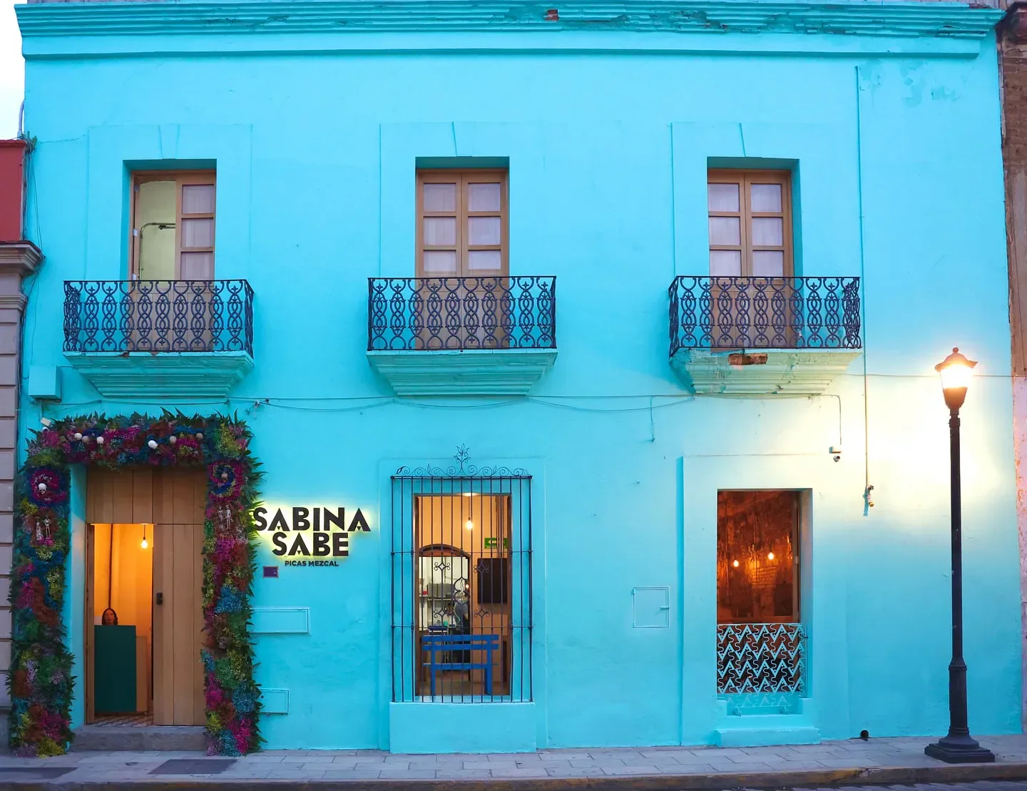 Exterior of Sabina Sabe restaurant in Oaxaca, featuring vibrant turquoise facade and flower decor.