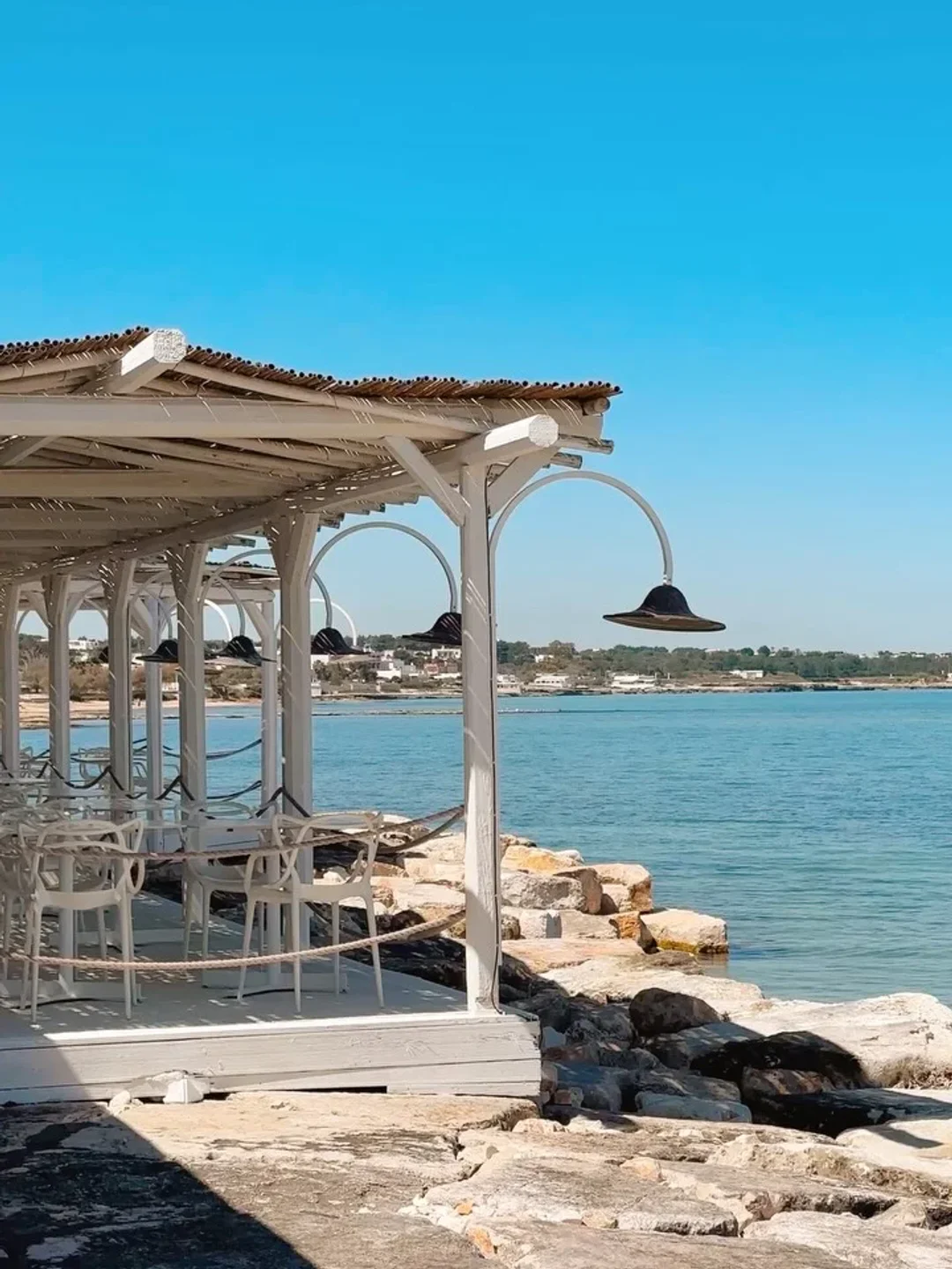 SaleBlu restaurant in Puglia offers beachfront dining with white tables and a thatched roof overlooking the sea.