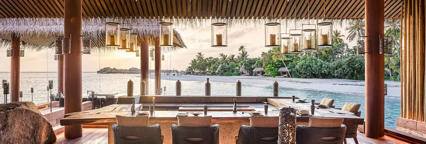 Dining area at Saoke in the Maldives, beachfront with island views and candle lanterns.