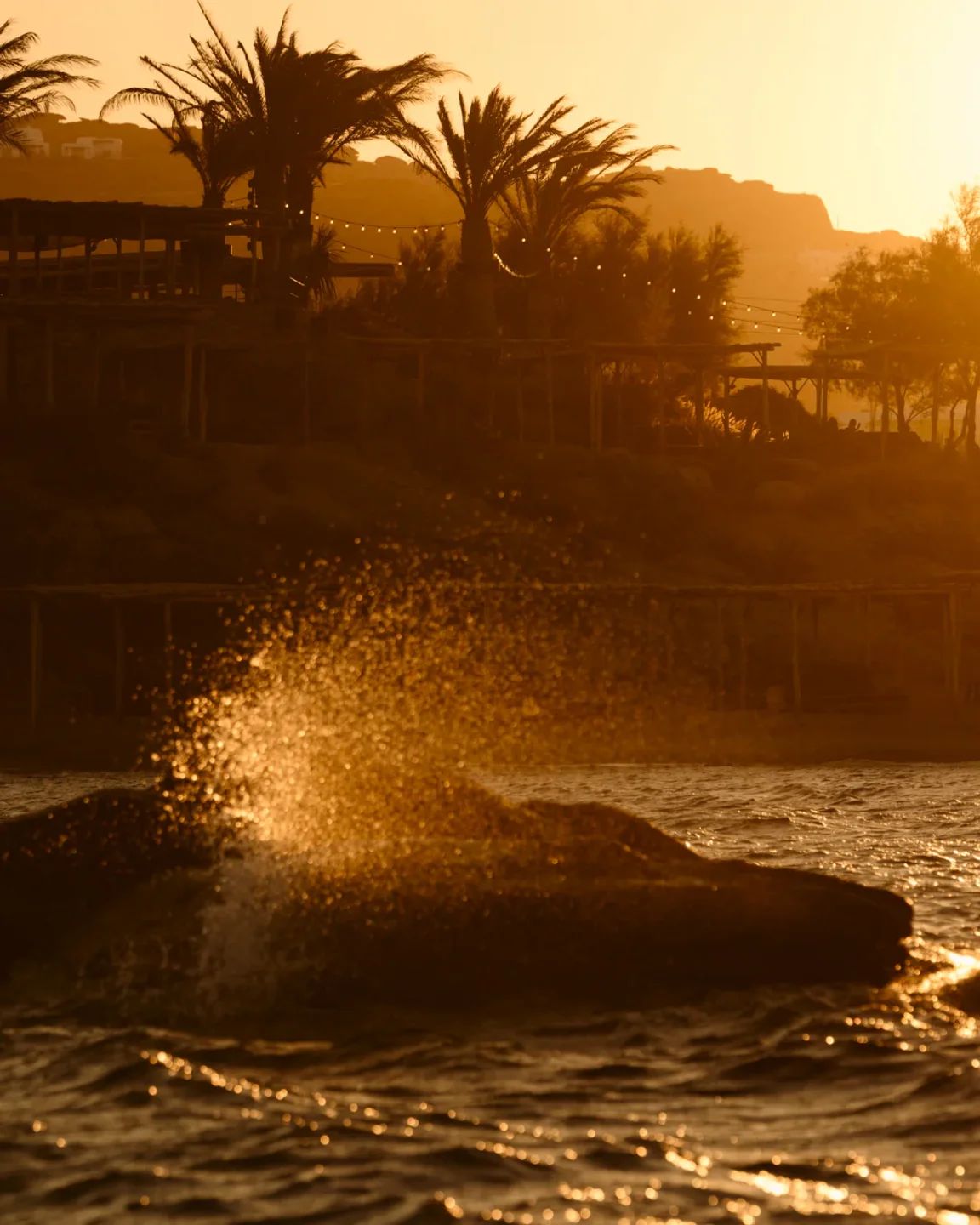 Golden hour sunset over the ocean waves and palm trees at Scorpios Mykonos