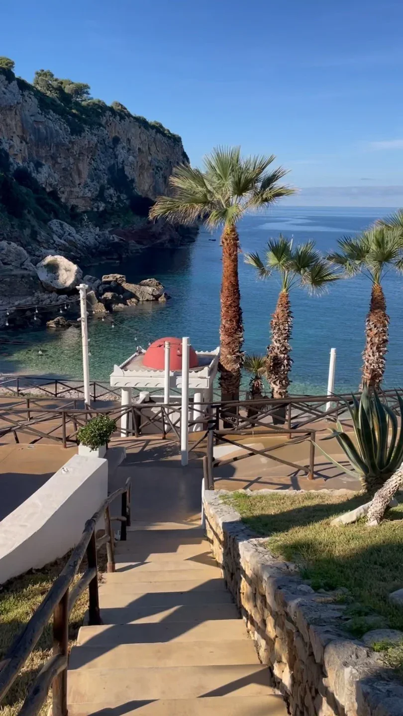 Scenic view of Sea Club Terrasini beach club in Sicily with palm trees and clear blue water.