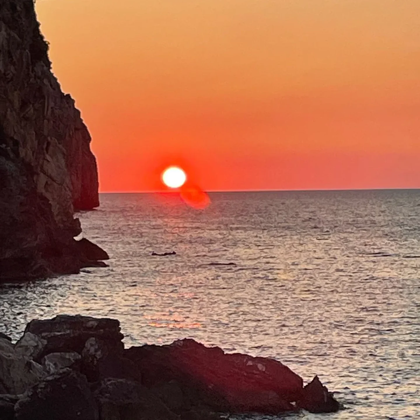 Dramatic sunset over the sea viewed from Sea Club Terrasini, Sicily, with rocky cliffs.