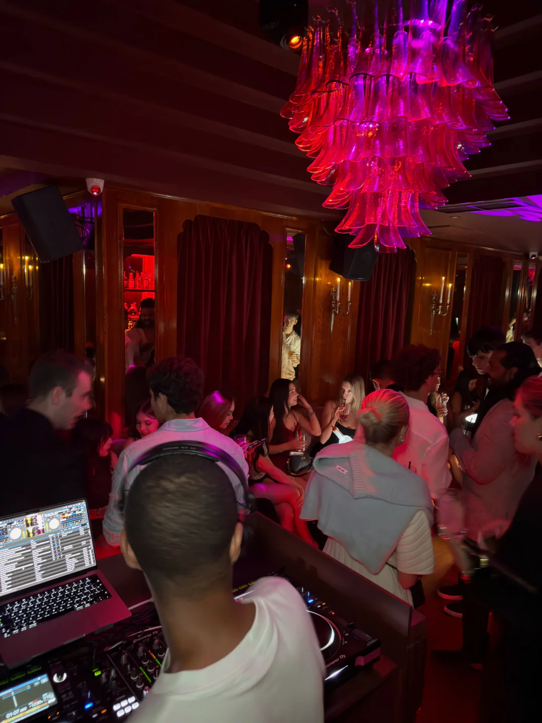 People enjoying the vibrant atmosphere at Selene Club, London, with a DJ setup and striking pink chandelier.