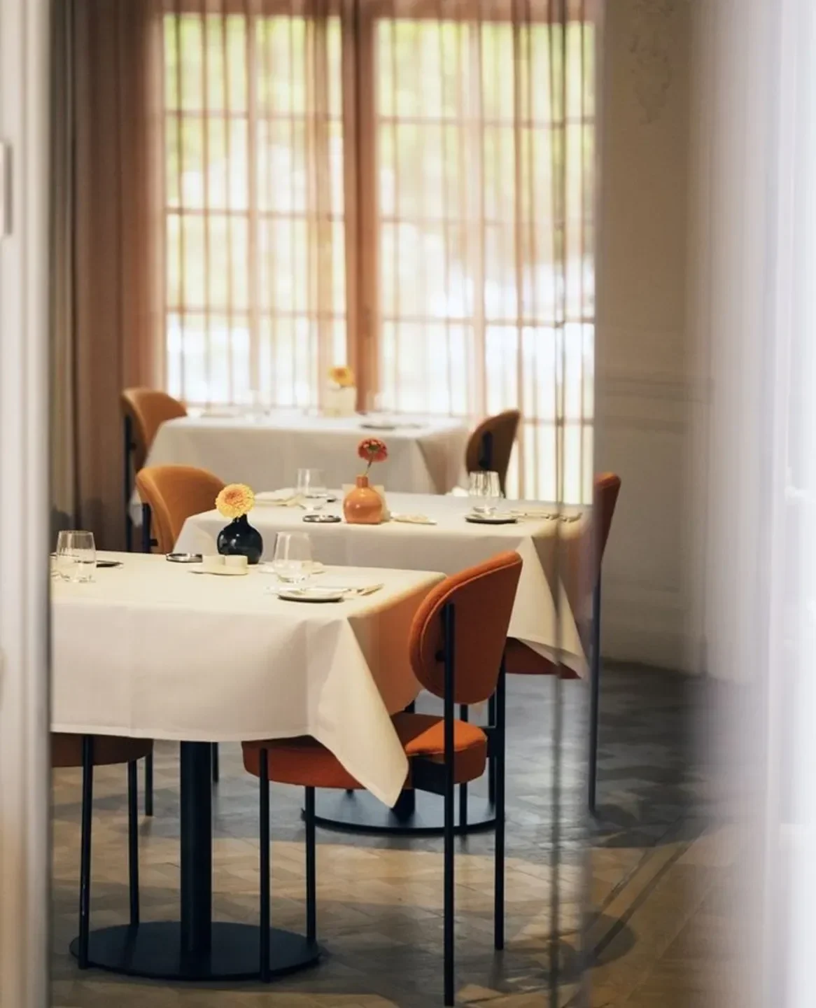 Elegant dining tables at Sensum restaurant in Ghent, featuring orange chairs and floral accents