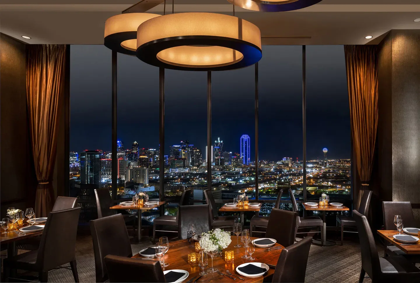 SĒR Steak Spirits in Dallas with a stunning city view at night from the dining room.
