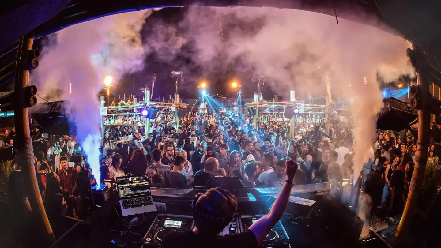 Energetic crowd at Shalvata nightclub in Tel Aviv with DJ and smoke effects.