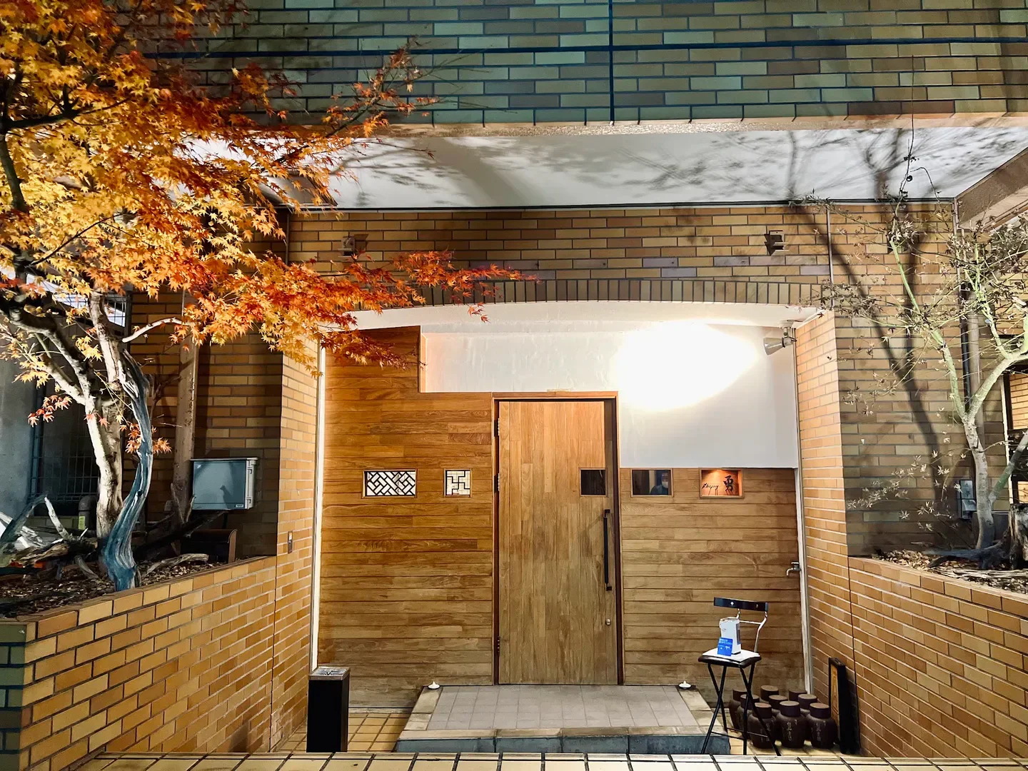 Entrance of Shichubo Yung restaurant in Tokyo, showcasing wooden door and autumn foliage.